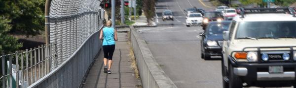 A woman jogging safely on a sidewalk beside a busy street.