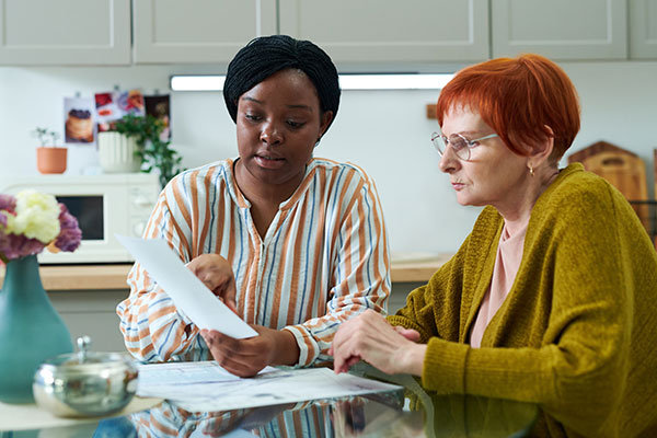 volunteer sitting at kitchen table together with senior woman and helping with insurance