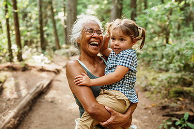 A grandma laughts while holding her granddaughter on a hike