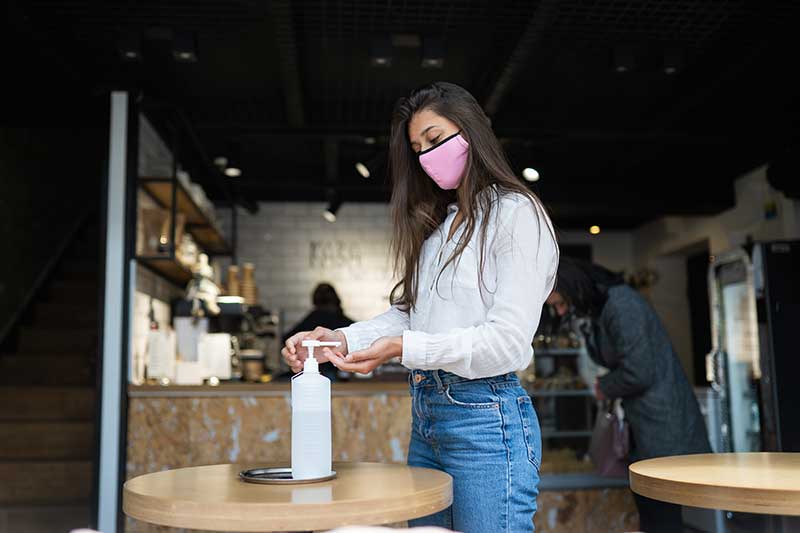 Woman wearing mask and using hand sanitizer at a business