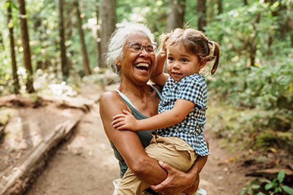 A grandma laughts while holding her granddaughter on a hike