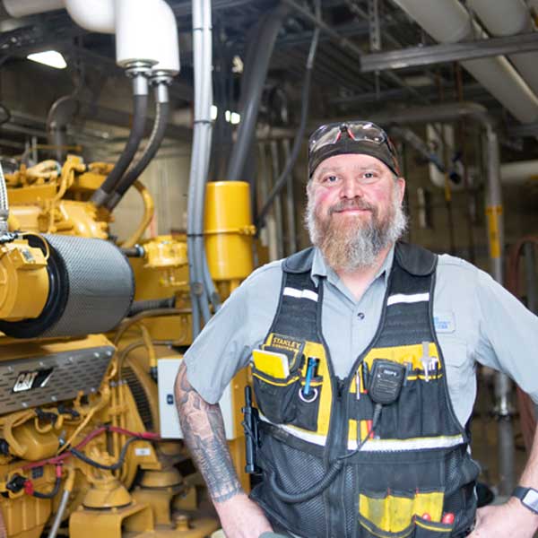 Man with safety equipment and tools stand in front of machinery